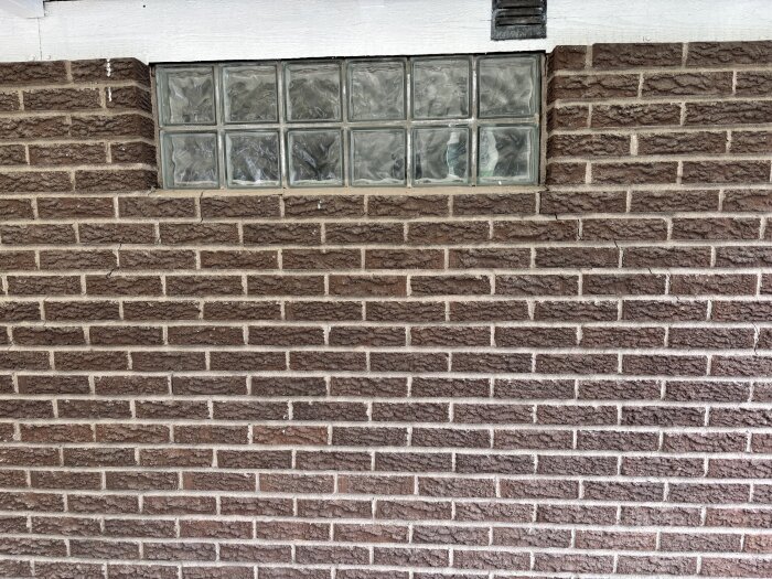 Tegelvägg med glasblocksfönster och flera synliga sprickor i murverket.
