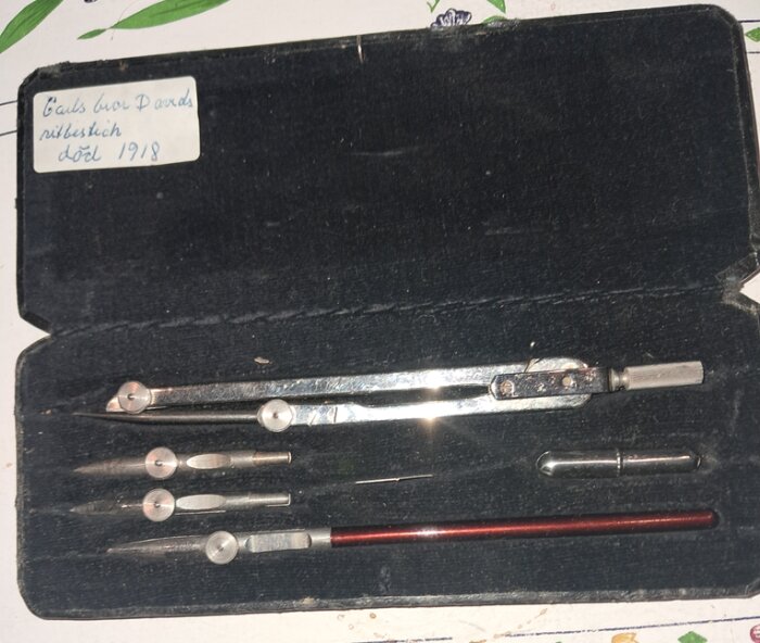 Gammalt ritverktygssats i svart fodral med passare och olika ritspetsar. Anteckning längst upp med text om bror död 1918.