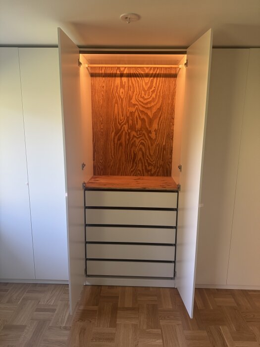 Vit garderob med öppna dörrar, innehållande IKEAs Komplement-lådor, en hylla och klädstång av oljat furu, saknar fortfarande golvlist.