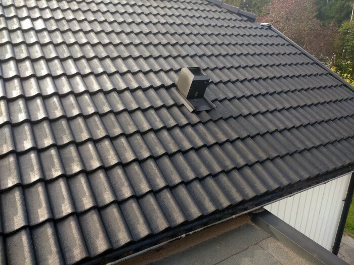 Nyrenoverat tak med svarta betongpannor som fått ett jämnt färglager. Skuggor syns på taket, vilket bidrar till tydliga kontraster.