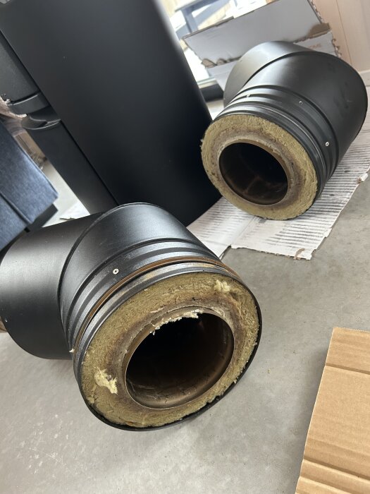 Svarta 45-graders böjar för en kamin installerade med isolering syns liggande på golvet, del av ett byggprojekt för en premodulskorsten.