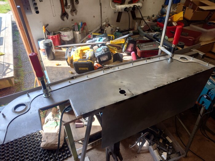 Arbetsbänk med halvfärdig aluminiumsvetsning, omgiven av verktyg och utrustning i en verkstad.