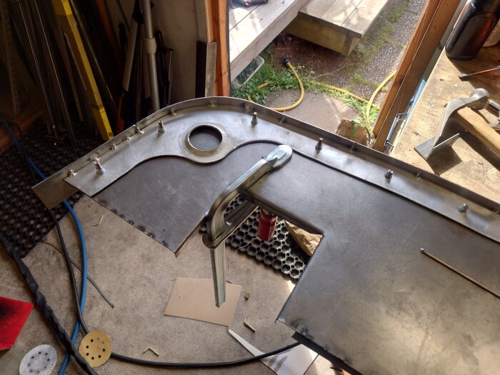 Aluminiumdel i verkstad, fastklämd för svetsning med flera skruvar och verktyg runt.