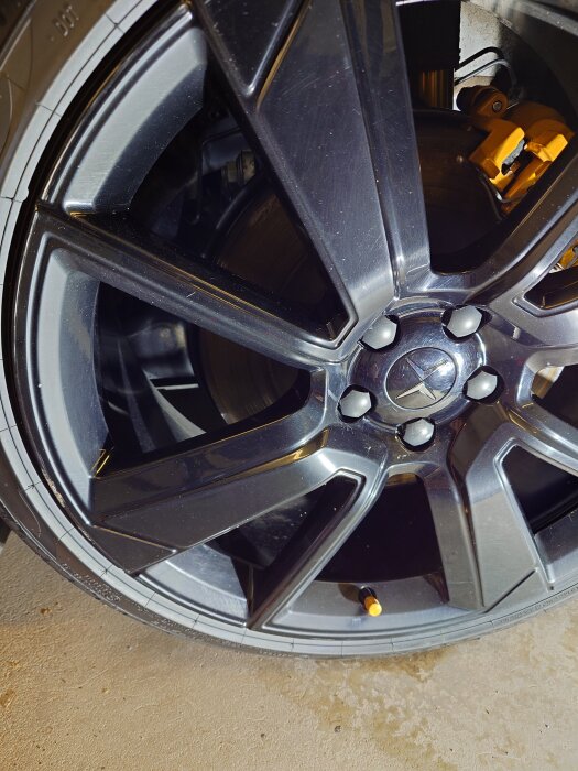 Svart bilfälg med guldfärgad bromsok bakom, matta ytor som visar oxidation före polering.