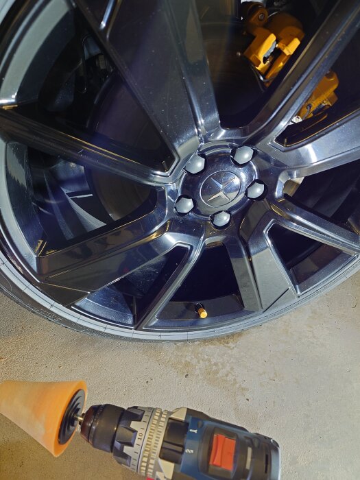 Svart bilfälg med polerkon monterad på en skruvdragare i förgrunden, redo för polering.