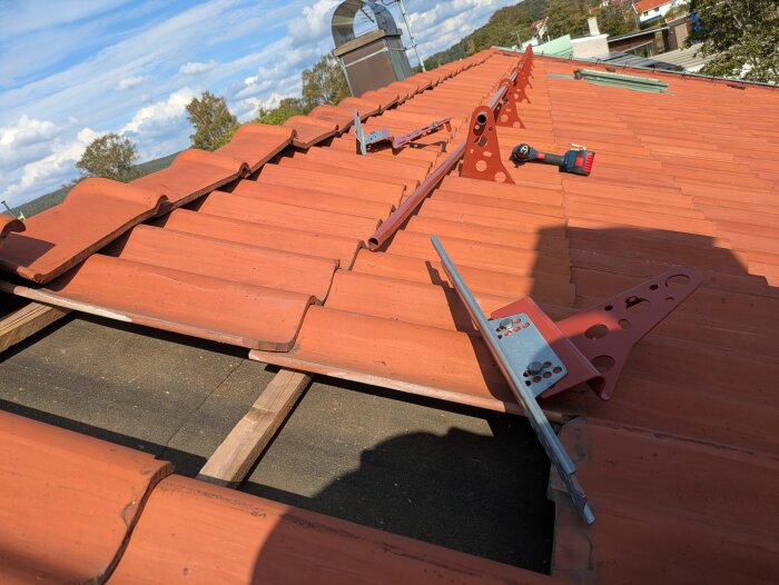 Rött tegeltak med monterat nockräcke, blå himmel i bakgrunden.