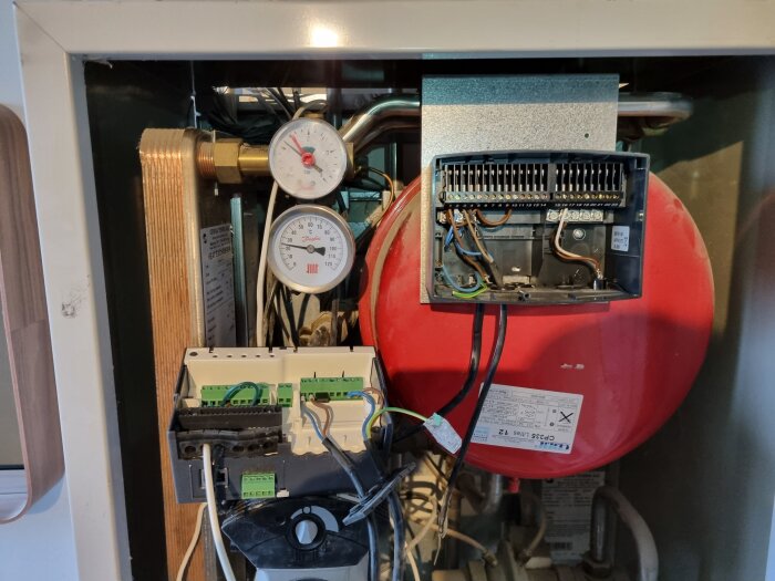 Inre komponenter av en värmepanna med två tryckmätare, kablar och en styrbox, delvis organiserade och anslutna.