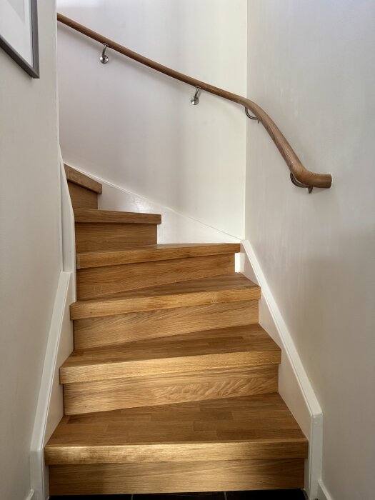 Trapp med nyligen installerat måttbeställt trappräcke i ljust trä mot ljus vägg.