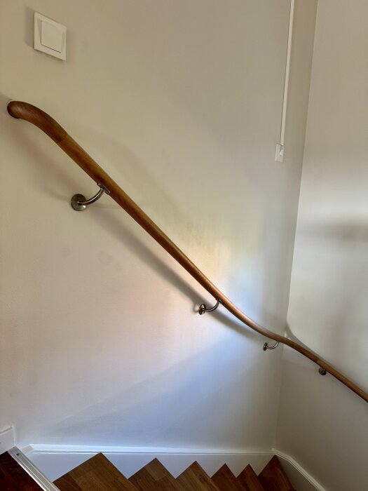 Måttbeställt trappräcke i trä monterat längs en vit vägg ovanför en trappa.