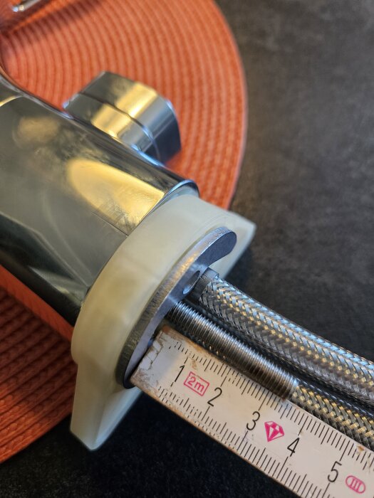 Närbild på köksblandare med synliga plaststödplatta och korta pinnbultar, måttstock visar längdskillnad, problem vid installation.