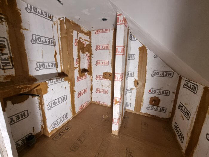Renovering av ett badrum med isoleringsmaterial markerat "HEY’DI" på väggarna och golvet i ett pågående byggprojekt.