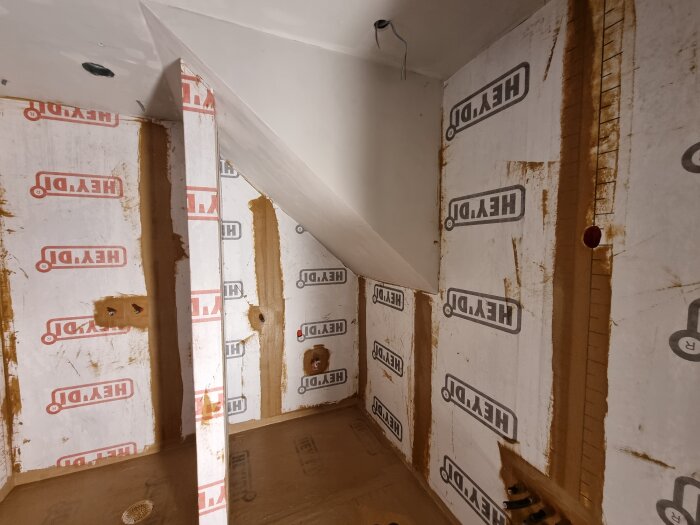 Badrum under renovering med våtrumsskivor märkta "HEY'DI" på väggarna och öppningar för vattenrör.