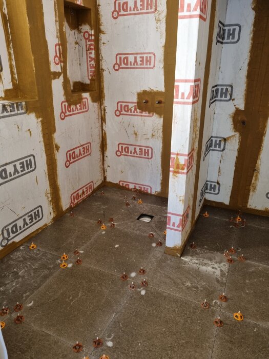 Badrumsrenovering med nylagda gråa klinkerplattor och väggar täckta av fuktspärr med logotypen "HEY'DI".