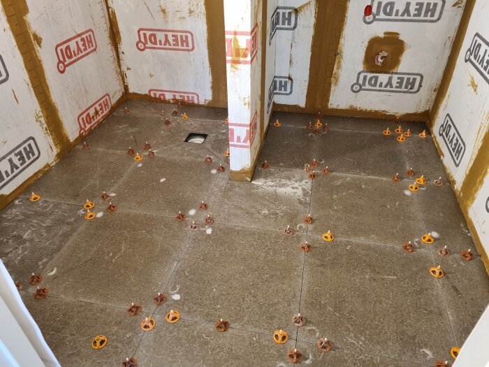 Badrum under renovering med nylagda kakelplattor och nivåjusteringsklossar på golvet.