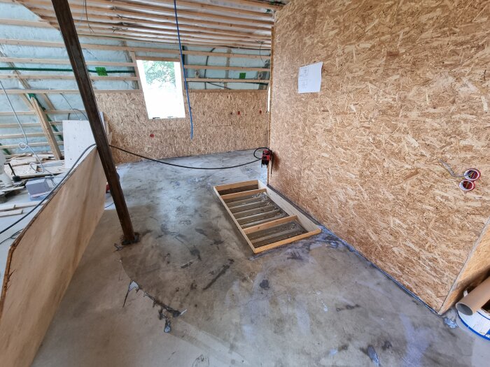 Byggarbetsplats för renovering av badrum, med träväggar och exponerad isolering. Träreglar och verktyg syns på golvet.