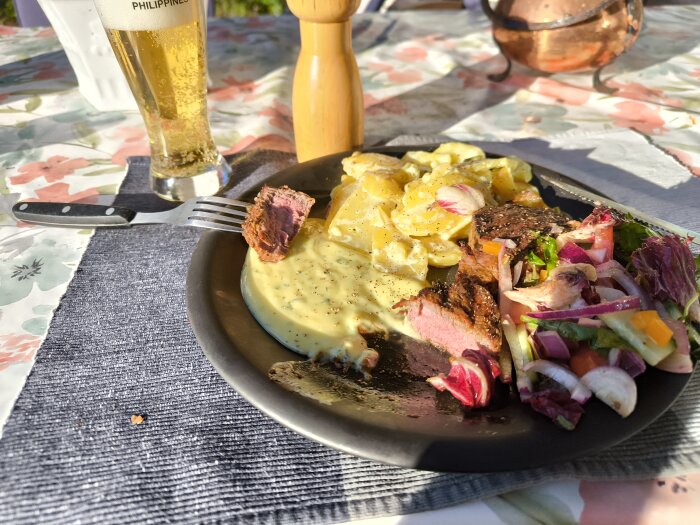 Grillad middag i kvällssolen med stek, sås, potatissallad och färsk sallad, serverad med öl på en uteplats.