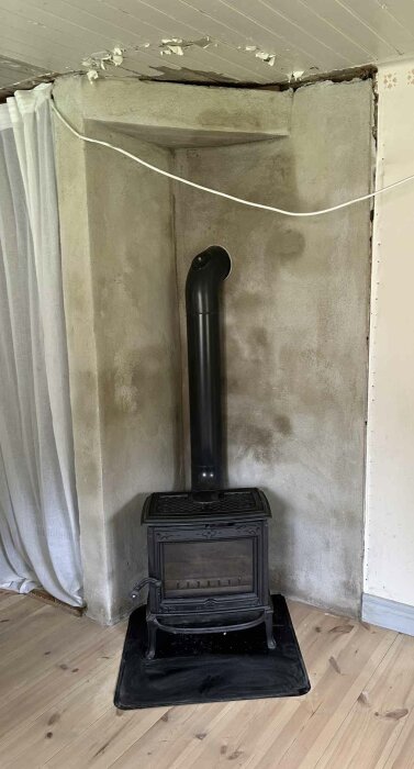 Renoverad murstock med kamin och rökrör, ståendes på svart skyddsplåt, omgivna av nylagt golv och väggar med breda takspringor.