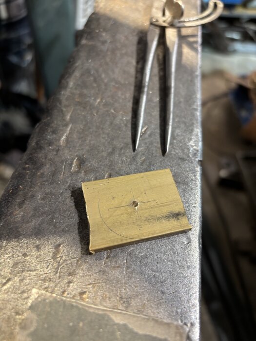 Metallkompass och mässingsplåt på arbetsbord i verkstad.