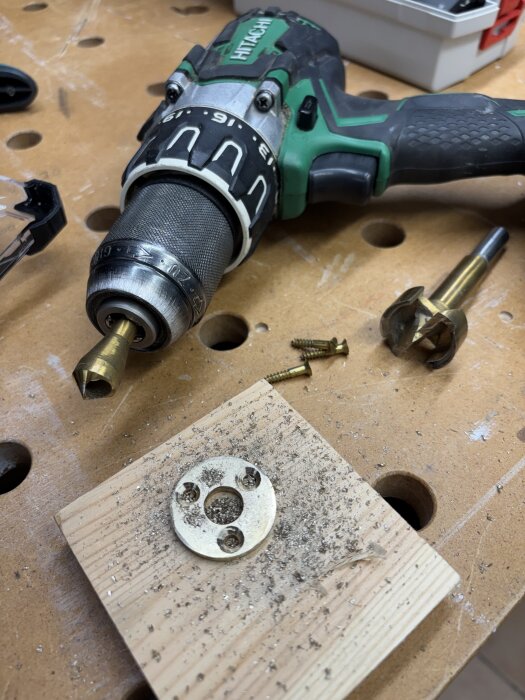 Borrmaskin och trähålskiva med metallbeslag och träspån, verktyg och skruvar på arbetsbänk för justering av dörrstängningsprojekt.