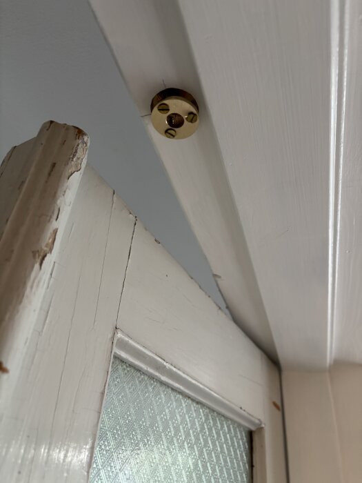 Vit trädörr med glasfönster, stängt ordentligt med metallögla på dörrkarmen för att säkerställa funktionalitet i gästrum/arbetsrum.