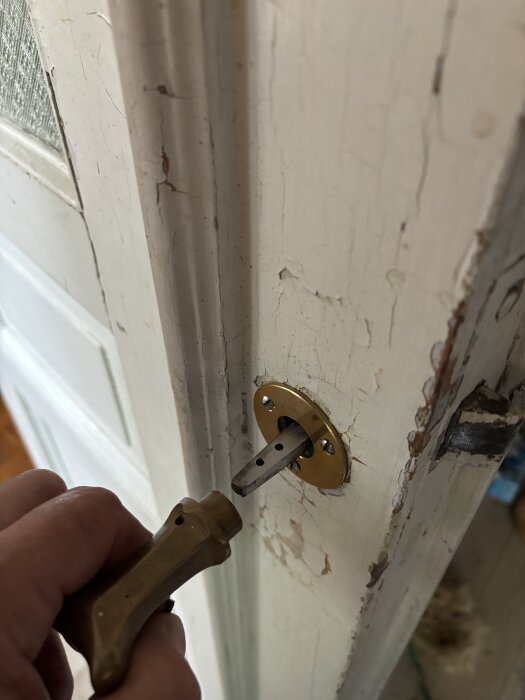 Hand justerar ett gammaldags dörrlås på en sliten vit dörr till gäst/arbetsrum.