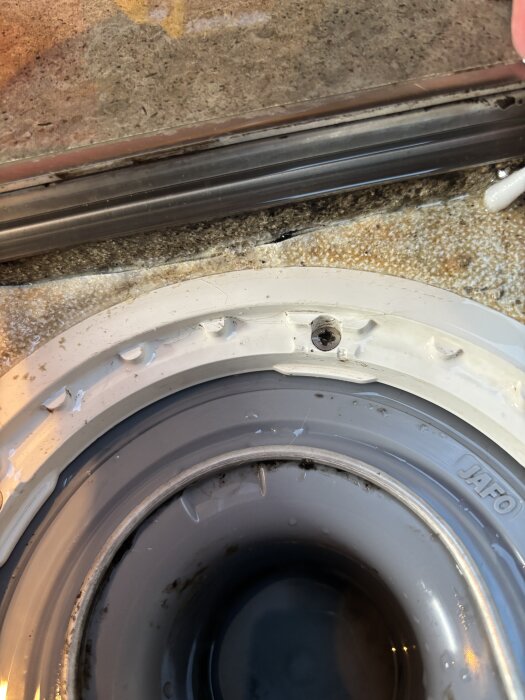 Sprucken golvbrunn med sprickor i tätskiktet bredvid. En tops pekar på skadan på tätskiktet kring brunnen.