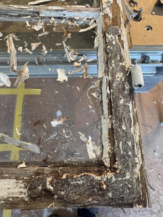 Gammalt färgborttaget gångjärn med rostig och sliten träram, träflisor och färgrester synliga runt kanten innan renovering.