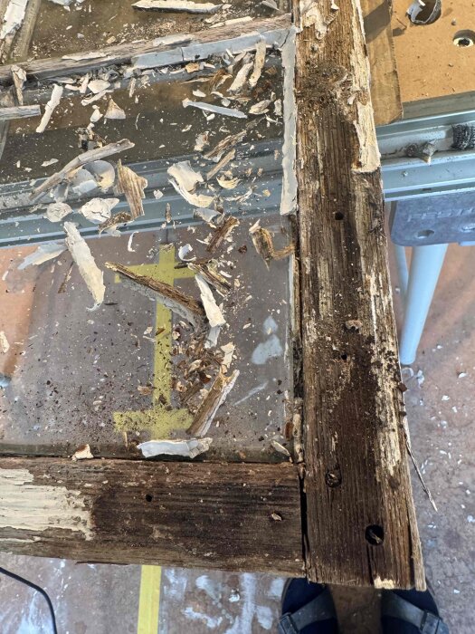 Gammalt trä med bortskrapad färg och synligt slitage, ligger på en arbetsyta täckt med flisor och skräp från renovering.