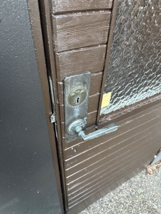 Ytterdörr med monterat metallhandtag och nyinstallerat lås, brun färg och räfflad yta.