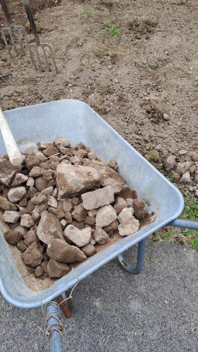 Skottkärra full med små och stora stenar framför en jordig yta.
