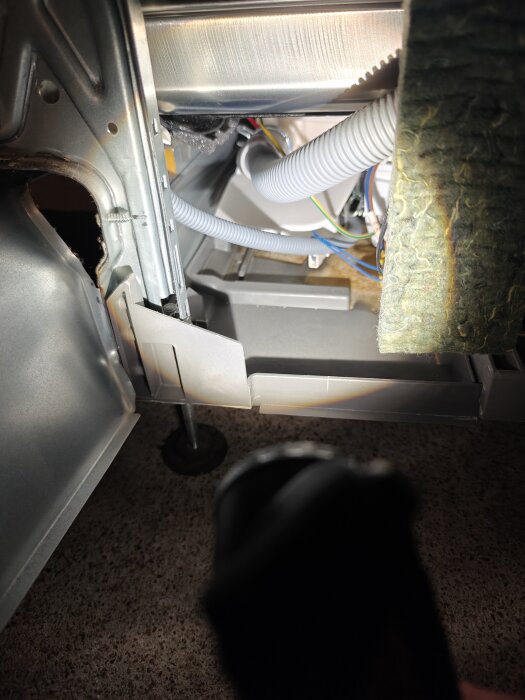 Insidan av en diskmaskin med synliga slangar och kablar, belysning från en ficklampa.
