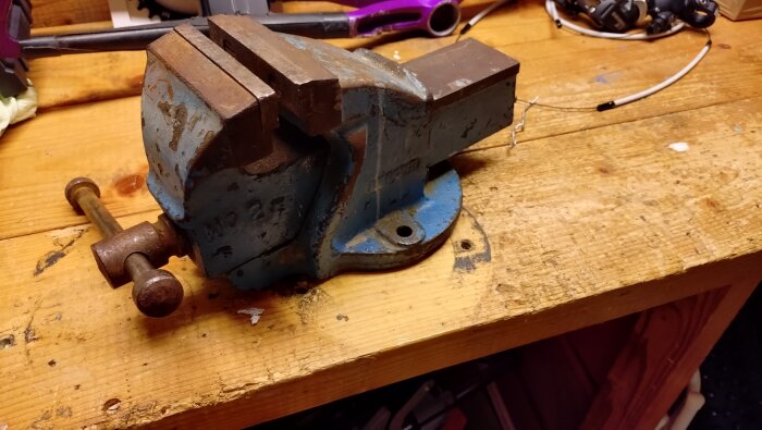 Ordentligt blått skruvstäd på en träbänk i ett garage.