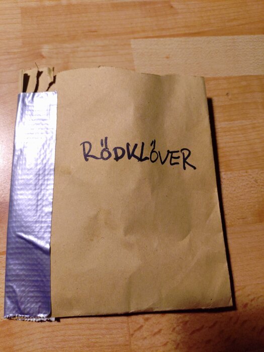 Brunt papperskuvert märkt "Rödklöver" på ett träbord.