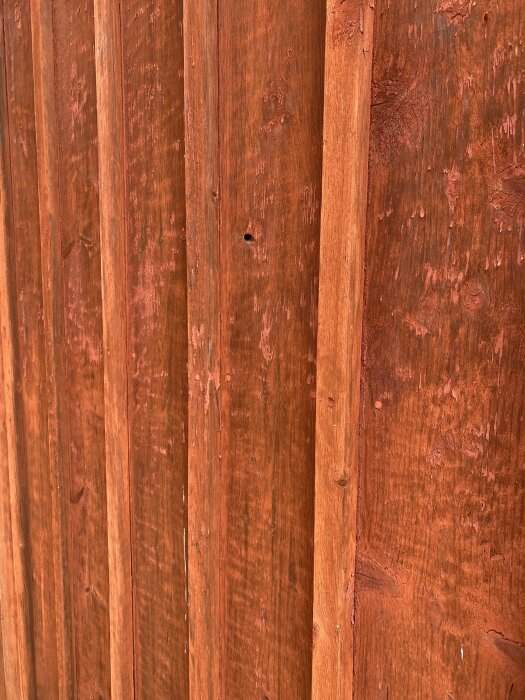 Närbild på träfasad, orangebrun nyans med vertikala panelbrädor och tydlig struktur, potentiellt för frågeställning om lockläkt.