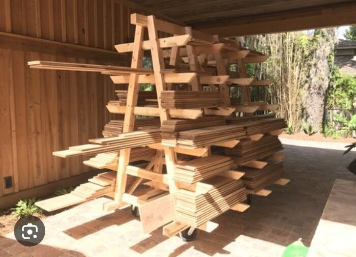 Trähylla i flervåningsstativstil med räta vinklar, fylld med träplankor, placerad i en täckt utomhusmiljö.