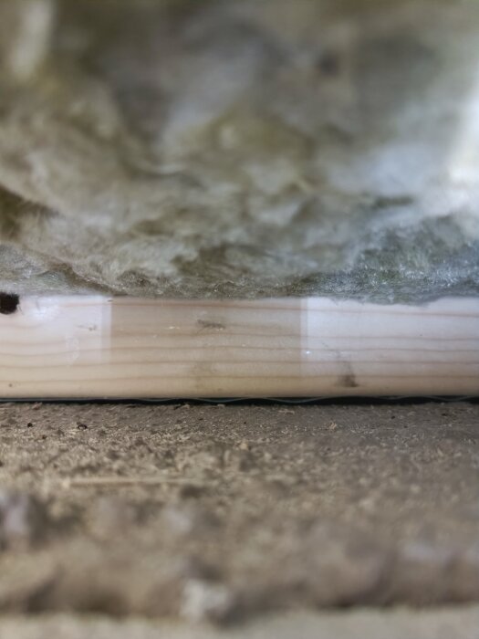 Isoleringsmaterial och träregel i en källare med synlig glespanel.