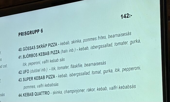 Meny för pizzor i prisgrupp 6 med olika ingredienser som kebab, skinka, pommes frites, isbergssallad, gurka, tomater, fläskfilé och bearnaisesås. Pris 142:-.