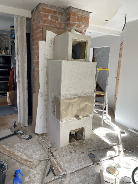 Kalciumsilikatblock staplade vid en exponerad tegelvägg under renovering, omgivna av verktyg och stökigt golv.