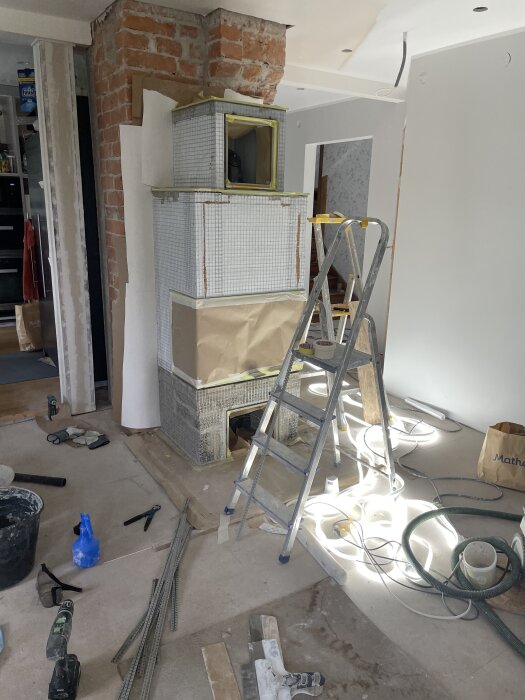 Byggarbetsplats med en halvfärdig murad vägg, byggställning, verktyg och byggmaterial spritt runt omkring.