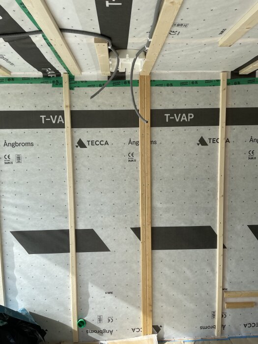 Vägg och tak med läkt och ångbroms, kablar hänger från taket i ett rum under renovering, plats för glasvägg markerad med dubbel läkt.