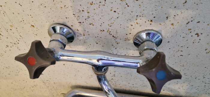 Gamla tvättställsblandaren med två vred, monterad på en spräcklig vägg, visar kopplingspunkterna till inkommande vattenrör.