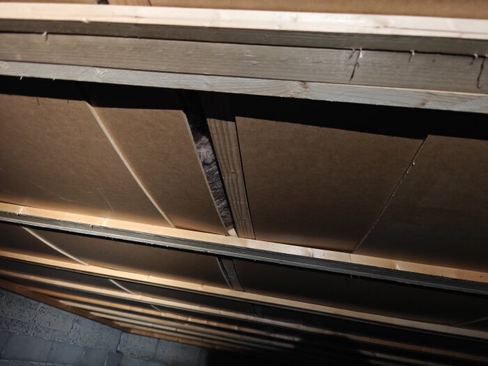 Krypgrundens undersida med masonitskivor som är böjda nedåt och visar glipor, potentiellt problem vid inspektion av husets grund.