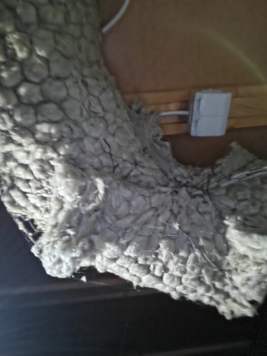 Närbild av isolering och elkablar i en krypgrund. En vit elanslutning syns mot en masonitskiva i bakgrunden.