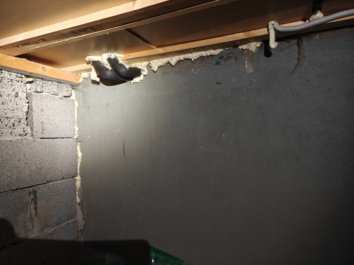 Svarta isolerade rör för golvvärme vidvägg, bredvid eluttag och ventilationskanal, synliga i takvinkeln ovanför betongblock.