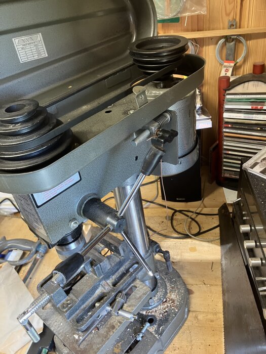 En bild av en pelarborrmaskin i en verkstad, omgiven av olika verktyg och material.