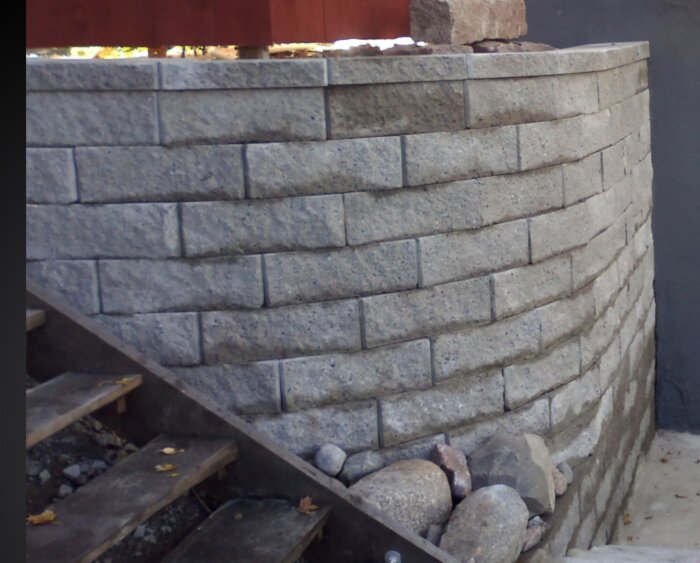 En två meter hög mur byggd av block med stenar vid basen, beskrivet som konstruerad med geonät och bergkross.