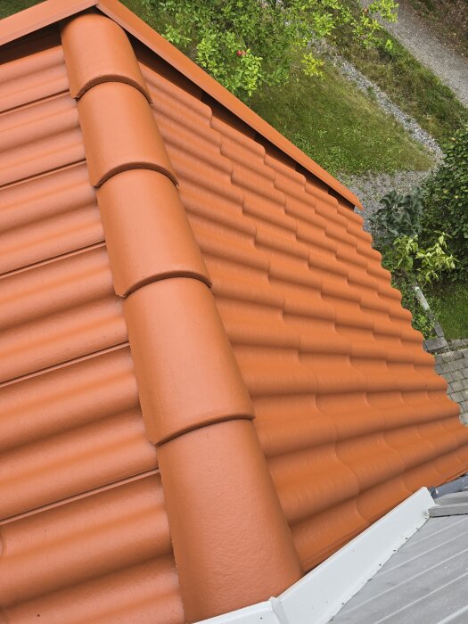 Nyrenoverat rött tak av tegelpannor med ny målarfärg sett från ovan, omgiven av grönska.