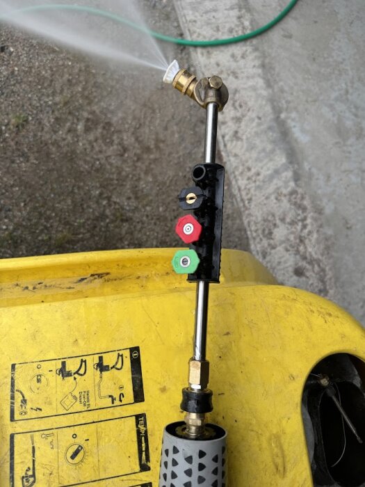 Hetvattentvätt på gul yta med läckage i led och skarv, tre munstycken i olika färger, vatten sprutar från ena munstycket.