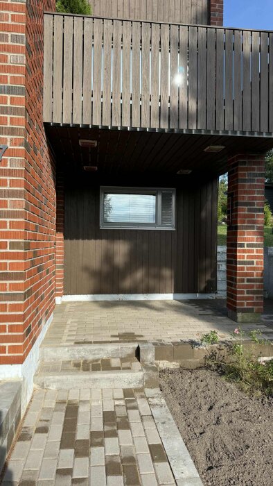 Trädgårdsgång med plattor och en liten trappa vid ett hus med tegelvägg och träpanel, oro över hala kanter vintertid.