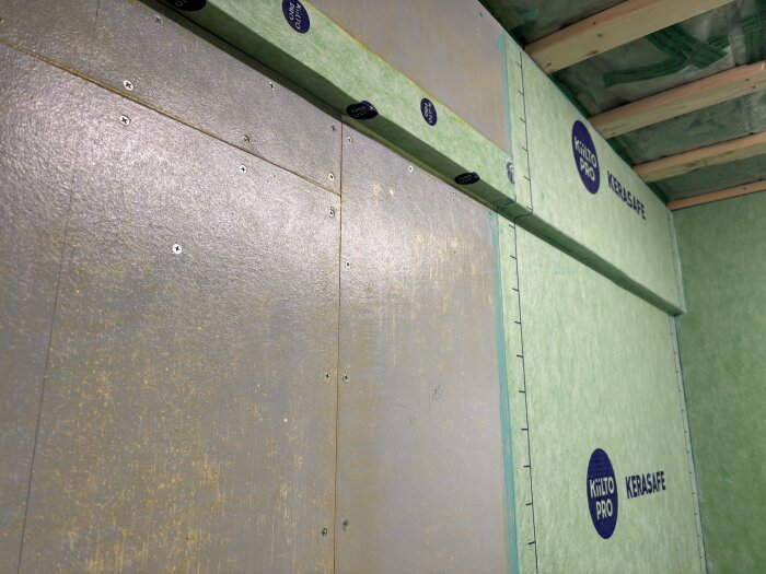 Tätskiktsfolie omger en balk i ett badrum under renovering. Folien är noggrant fixerad med skruvar på väggbeklädnaden.